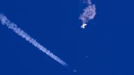 In this photo provided by Chad Fish, the remnants of a large balloon drift above the Atlantic Ocean, just off the coast of South Carolina, with a fighter jet and its contrail seen below it, Saturday, Feb. 4, 2023. The downing of the suspected Chinese spy balloon by a missile from an F-22 fighter jet created a spectacle over one of the state...s tourism hubs and drew crowds reacting with a mixture of bewildered gazing, distress and cheering. (Chad Fish via AP)