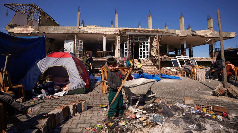 Families sit next to a destroyed building in Antakya, southern Turkey