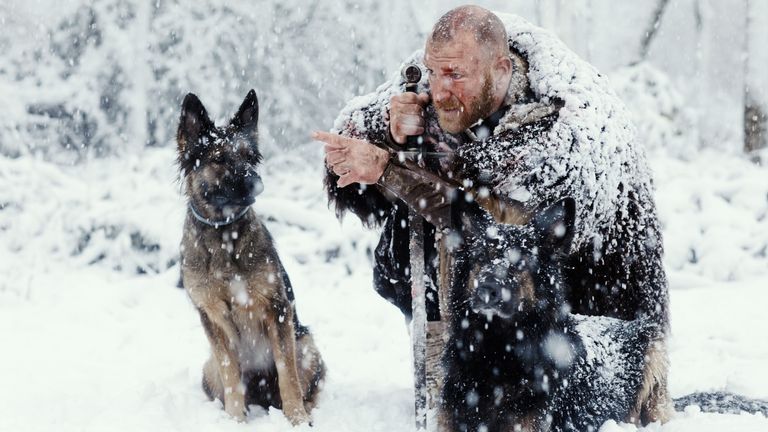 Bloody viking warrior in a winter snowstorm with hunting dogs