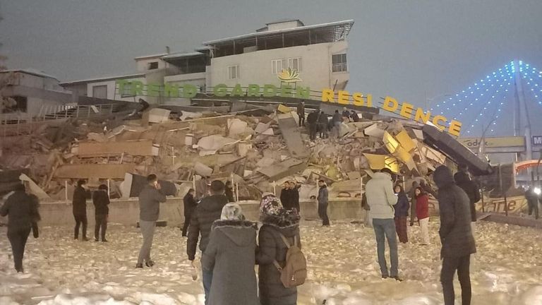 People stand in front of a collapsed residential building after an earthquake in Malatya, Turkey