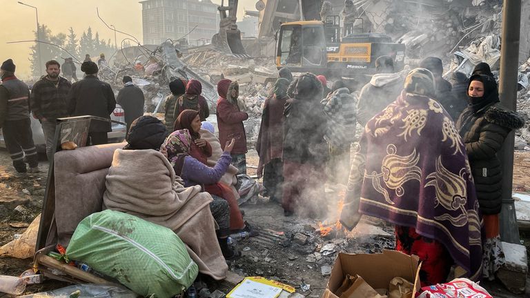 Türkiye'nin güneyindeki Hatay'da meydana gelen yıkıcı depremin ardından çöken bir binanın yakınındaki yangının etrafında toplanan vatandaşlar.