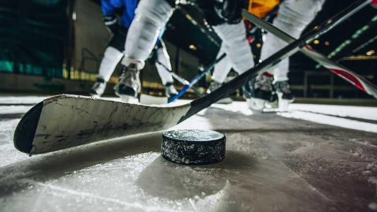 Close up of hockey puck and stick during a match with players in the background. (iStock)