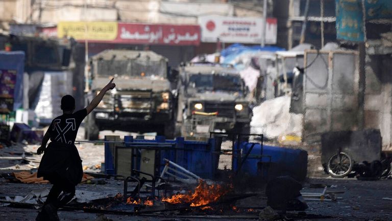 A Palestinian gestures to Israeli military vehicles during clashes in the West Bank city of Nablus, Wednesday, Feb. 22, 2023. Israeli troops moved into the city, setting off fighting that killed several Palestinians, including a 72-year-old man, Palestinian health officials said. The Israeli military gave few details about its operation in the northern city, which is known as a militant stronghold, and the army frequently operates there. (AP Photo/Majdi Mohammed)