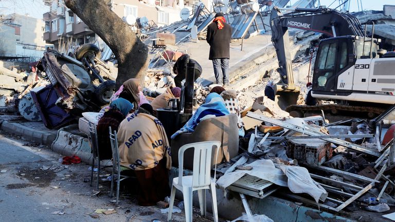 People sit next to a collapsed building following an earthquake in Kahramanmaras, Turkey February 8, 2023. REUTERS/Dilara Senkaya