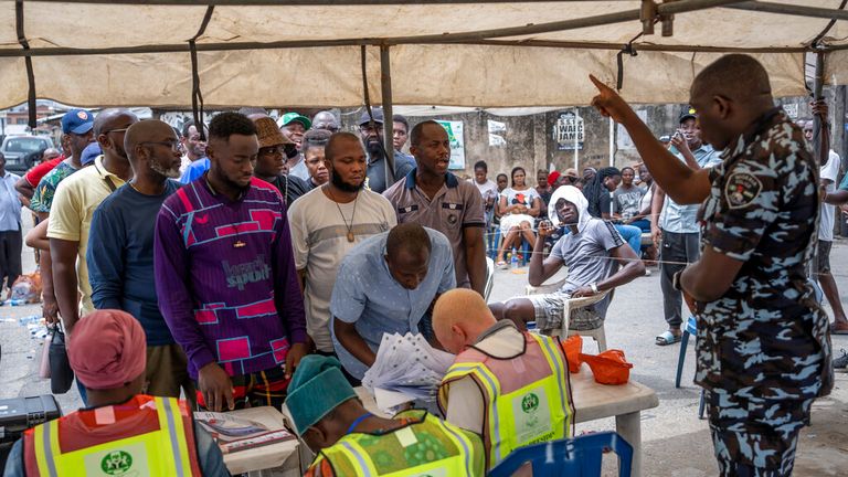 Ein Polizist fordert einen Mann auf, sich nach hinten zu stellen, während sich die Wähler in Lagos, Nigeria, anstellen, um ihre Stimmzettel abzugeben 