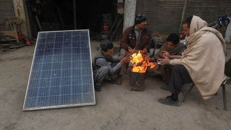 People warm themselves by a fire beside a solar panel, a day after a country-wide power breakdown, in Peshawar, Pakistan, January 24, 2023. REUTERS/Fayaz Aziz