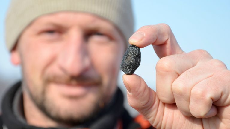 A local resident shows a fragment thought to be part of a meteorite collected in a snow covered field in the Yetkulski region outside the Urals city of Chelyabinsk February 24, 2013. A meteor that exploded over Russia&#39;s Ural mountains and sent fireballs blazing to earth has set off a rush to find fragments of the space rock which hunters hope could fetch thousands of dollars a piece. REUTERS/Andrei Romanov (RUSSIA - Tags: SOCIETY SCIENCE TECHNOLOGY)