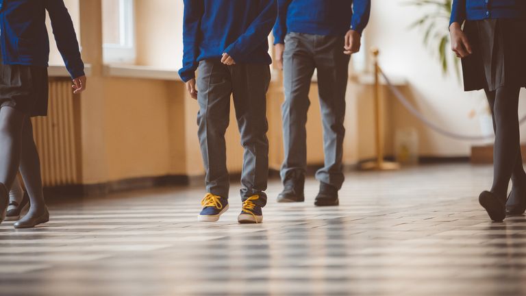 Schoolchildren walking in school corridor. Focus on legs of pupils walking through school hallway.