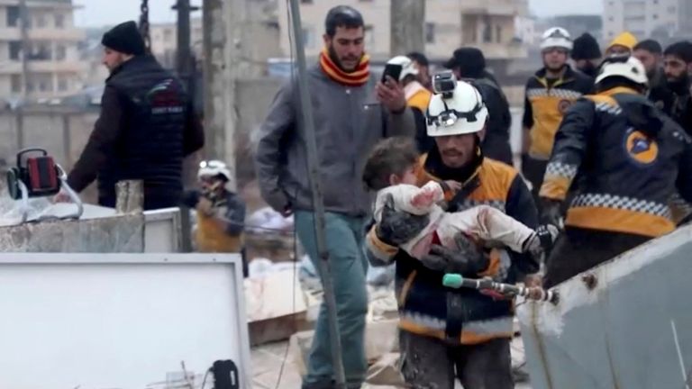 A rescuer carries an injured child away from the rubble of a building