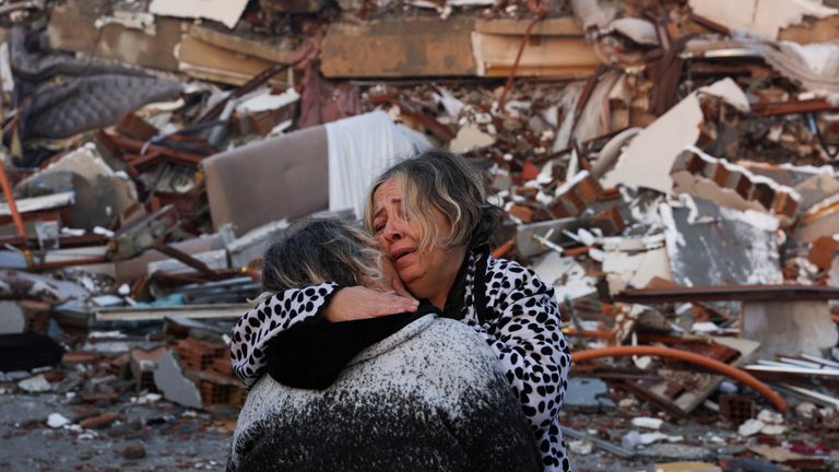 A woman reacts while embracing another person, near rubble following an earthquake in Hatay, Turkey