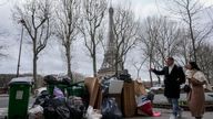 FILE- People walk past not collected garbage cans near the Eiffel Tower in Paris, Sunday, March 12, 2023. The City of Light is losing its luster with tons of garbage piling up on Paris sidewalks as sanitation workers strike for a ninth day. (AP Photo/Michel Euler, File)