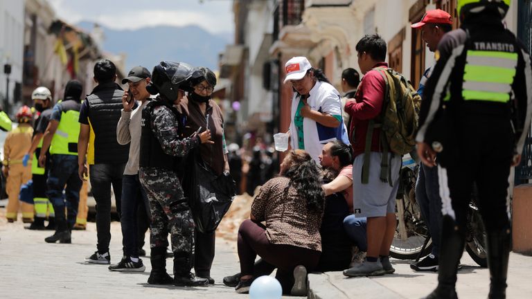 Police talks to people next to the site where a car was crushed by debris after an earthquake shook Cuenca, Ecuador