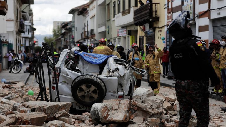 A police officer looks up next to a car crushed by debris after an earthquake shook Cuenca, Ecuador