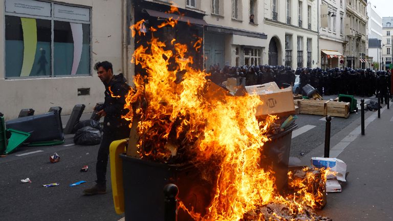 A protester walks past burning garbage bins as French riot police stand in position amid clahes during a demonstration as part of the ninth day of nationwide strikes and protests against French government's pension reform, in Paris, France, March 23, 2023. REUTERS/Gonzalo Fuentes