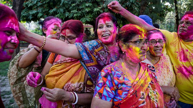 Elderly women smear colored powder on each other as they celebrate Holi.