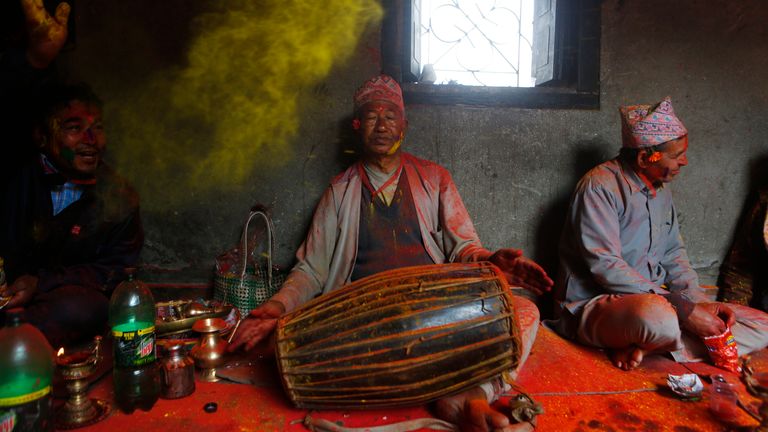 A Nepalese man throws color as a man plays traditional drum during Holi festival