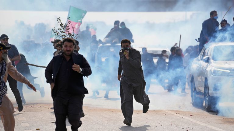 Supporters of former Prime Minister Imran Khan take shelter after police fired tear gas canisters to disperse them during clashes, in Islamabad, Pakistan on Saturday March 18, 2023. A Pakistani court of High level suspended an arrest warrant for former Prime Minister Khan, giving him a reprieve to travel to Islamabad and face charges in a corruption case without being detained.  (AP Photo/Anjum Naveed)