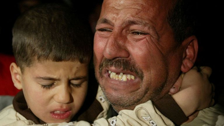 FILE PHOTO: An Iraqi man holds a young boy and cries in front of a house damaged by a missile during an airstrike in Baghdad, Iraq, March 22, 2003.REUTERS/Goran Tomasevic/File Photo Search "20th Anniversary of the US Invasion of Iraq" for photos
