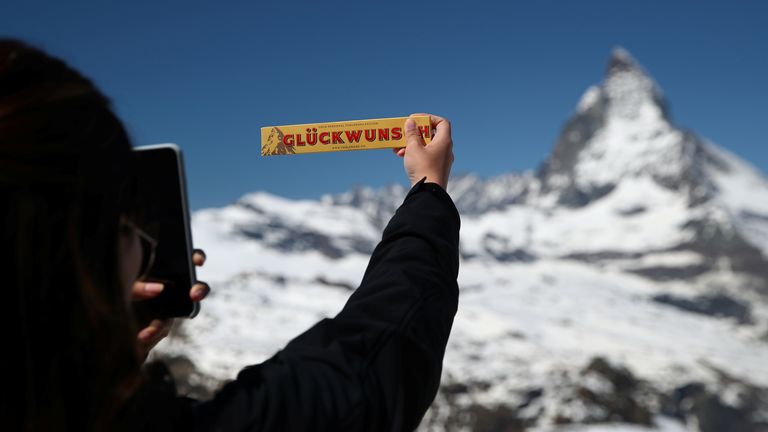 A tourist takes a picture of a Toblerone chocolate in front of the Matterhorn mountain at the Gornergrat in Zermatt, Switzerland June 2, 2019. The word on the box reads good whishes. REUTERS/Denis Balibouse