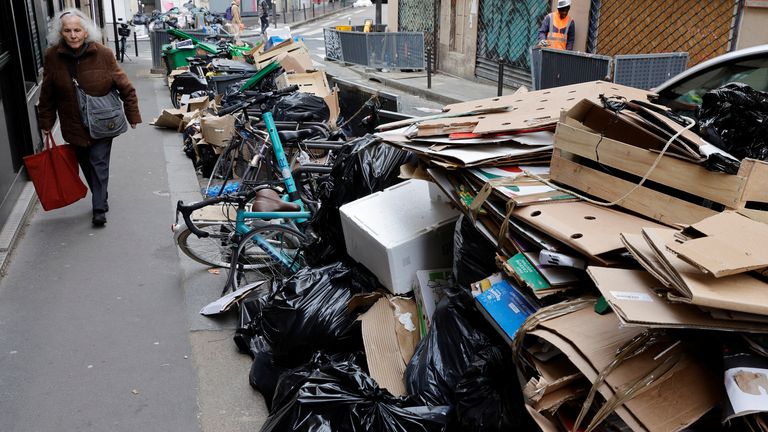 A woman walks past piles of garbage bags on a street as overflowing rubbish was not collected due to a garbage collectors' strike against the French government's pension reform, in Paris, France, March 17, 2023. REUTERS/Pascal Rossignol