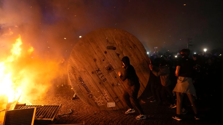 Göstericiler, 17 Mart 2023 Cuma günü Paris'teki bir protesto sırasında tahta bir kablo makarasını yanan bir barikata yuvarlarken. Resim: AP