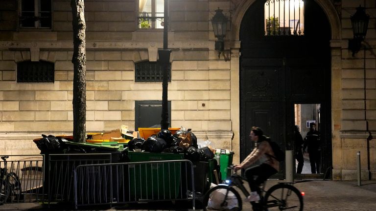 A man rides a bicycle past uncollected rubbish bins near the Elysee Palace in Paris, France, Monday, March 13, 2023. A controversial bill that would raise France's retirement age from 62 to 64 has been pushed by the Senate's passage of the measure amid strikes, protests and uncollected trash piling up day by day.  (AP Photo/Michel Euler)