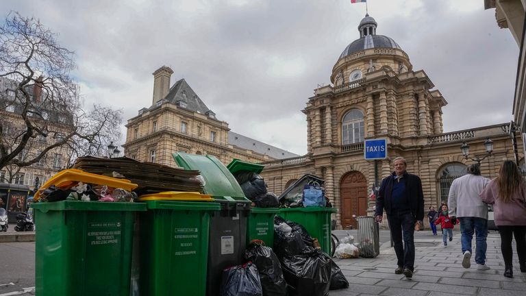 ARCHIVO- El domingo 12 de marzo de 2023, personas pasan frente a botes de basura sin recolectar junto al Senado en París.  La Ciudad de la Luz está perdiendo su brillo a medida que los trabajadores parisinos hacen huelga por noveno día y toneladas de basura se acumulan en las aceras de París.  (Foto AP/Michelle Euler, archivo)