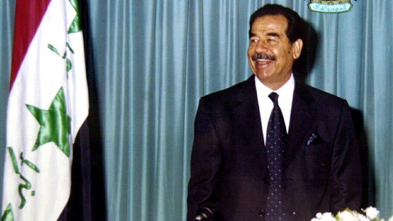 Irak Devlet Başkanı Saddam Hüseyin Irak bayrağının yanında duruyor, 17 Ocak 2002. Körfez Savaşı'nın 11. yıldönümünde, Başkan Saddam Hüseyin Perşembe günü ülkesinin savaşın bir parçası olarak Irak'a yönelik herhangi bir yeni ABD askeri saldırısına hazır olduğunu ve bunu engelleyeceğini söyledi. teröre karşı.  REUTERS/INA/POOL fk/CRB