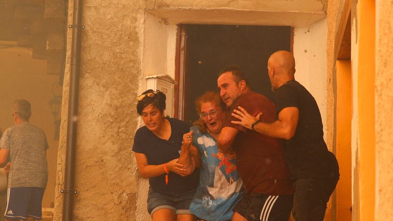 A woman is helped out of a house by neighbours in Anon de Moncayo, Spain on Saturday Aug. 13, 2022. A large wildfire in northeast Spain grew rapidly overnight and was burning out of control. It has already forced the evacuation of eight villages and 1,500 people in Zaragoza province. A local government official said Sunday that the situation was critical in the town of A..on de Moncayo and the priority for the 300 firefighters fighting the blaze was to protect human lives and villages. Pic: AP