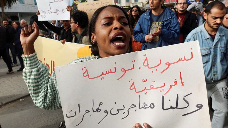 A pro-migrant protester holds a banner which reads "feminist, Tunisian, African"