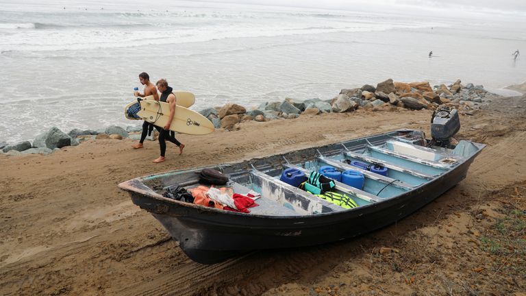 Surfers walk by a panga boat sitting along the Black&#39;s Beach, after two capsized off the coast of San Diego