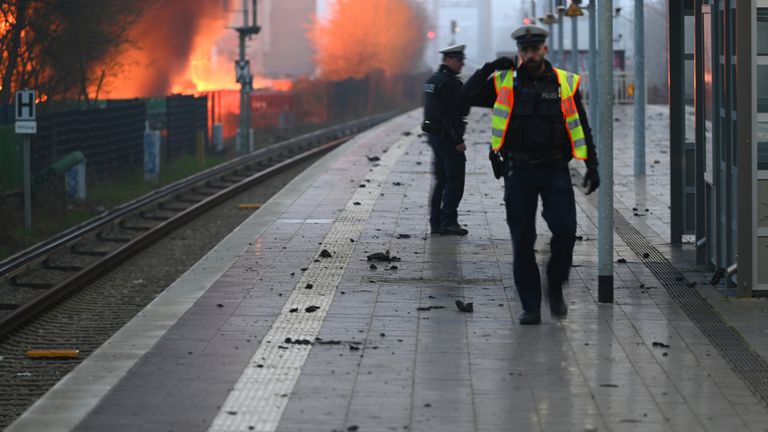 Police walk along the tracks of Hamburg-Rothenburgsort station, while flames of a large fire can be seen in the background. Pic: AP