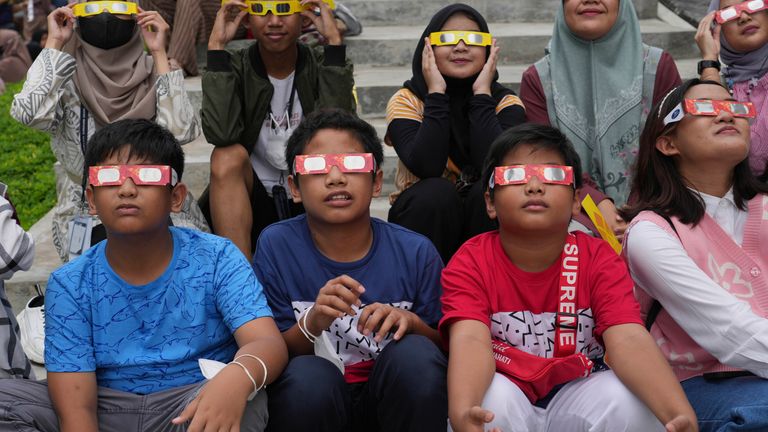 Endonezyalı gençler 20 Nisan 2023 Perşembe günü Endonezya'nın Jakarta kentinde güneş tutulmasını izlemek için koruyucu gözlük takıyorlar. Nadir görülen bir güneş tutulması Perşembe günü Avustralya, Endonezya ve Doğu Timor'un ücra bölgelerinin üzerinden geçecek.  (AP Fotoğrafı/Tatan Syuflana)