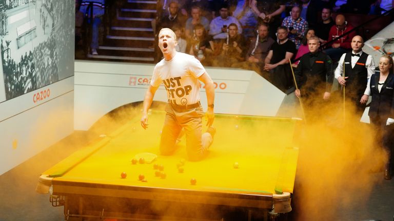 A Just Stop Oil protester jumps on the table and throws orange powder during the match between Robert Milkins against Joe Perry during day three of the Cazoo World Snooker Championship at the Crucible Theatre, Sheffield. Picture date: Monday April 17, 2023.