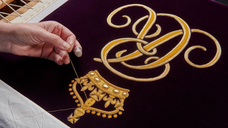 A member of the Royal School of Needlework hand embroidering the Queen Consort&#39;s cypher onto her Robe of Estate