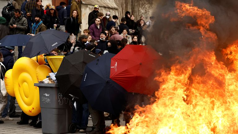 Masked protesters protect themselves with umbrellas near burning garbage bins amid clashes during a demonstration as part of the eleventh day of nationwide strikes and protests against French government&#39;s pension reform, in Rennes, France, April 6, 2023. REUTERS/Stephane Mahe
