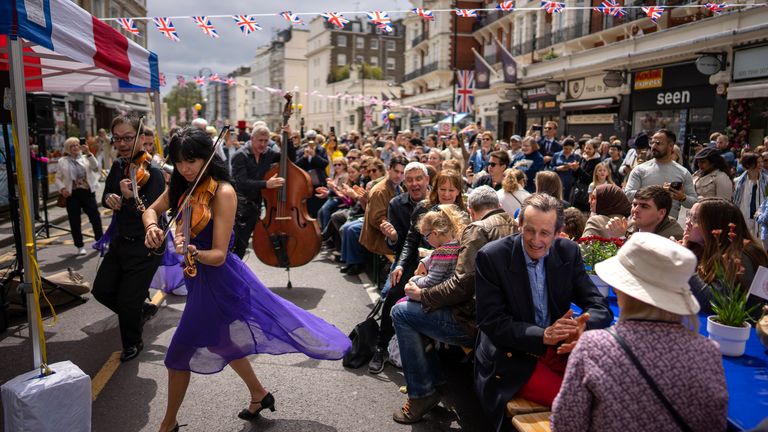 Musicians play their instruments as people sit at long tables to eat their lunch as part of the Big Lunch celebration in London 
Pic:AP