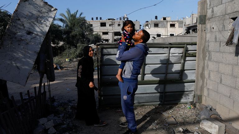 A Palestinian man carries his daughter as he returns to his damaged home