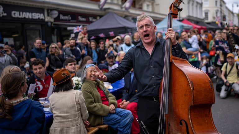 Musicians play their instruments as people sit at long tables to eat their lunch as part of the Big Lunch celebration in London
Pic:AP
