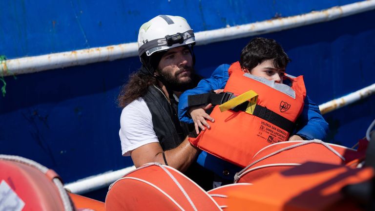 A member of MSF is carrying a little boy from the broken down fishing vessel onto the Rip that will take them back to the Geo Barents