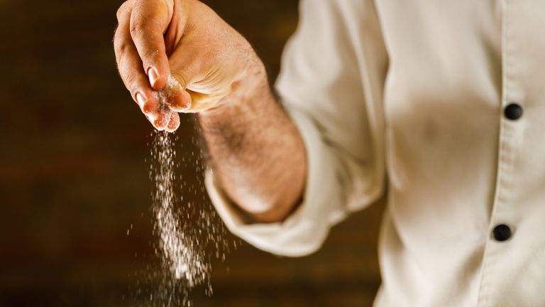 Close up of unrecognizable chef adding salt while preparing a meal in the kitchen.