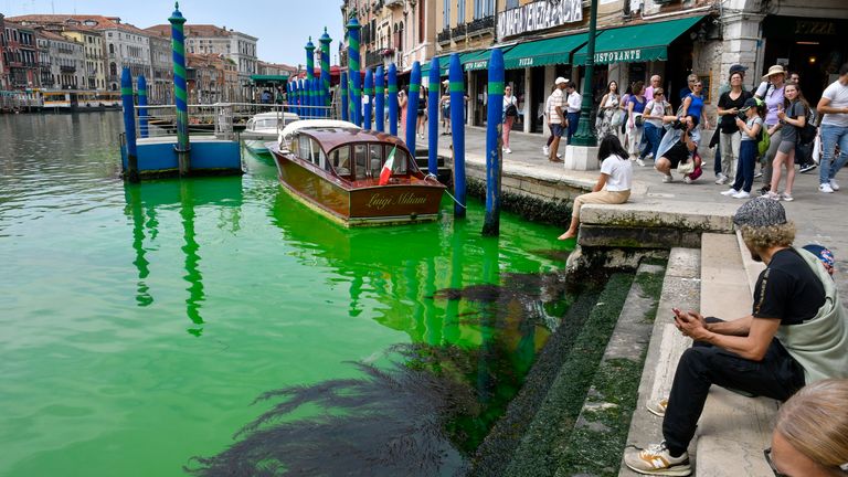 Oamenii privesc la Marele Canal istoric al Veneției în timp ce un petic de lichid verde fosforescent se răspândește în el, duminică, 28 mai 2023. Guvernatorul regiunii Veneto, Luca Zaia, a declarat că oficialii au cerut poliției să investigheze pentru a stabili cine era responsabil, deoarece autoritățile de mediu testau și apa.  (AP Foto/Luigi Costantini)
