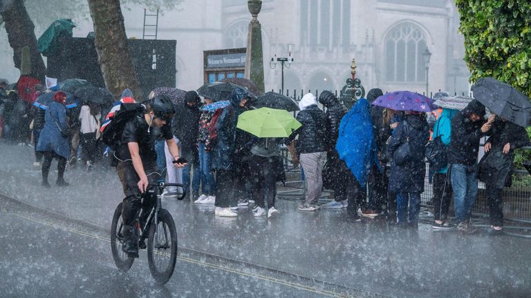 Pedestrians and royal fans are caught in a heavy downpour in Westminster a day before the coronation of King Charles III