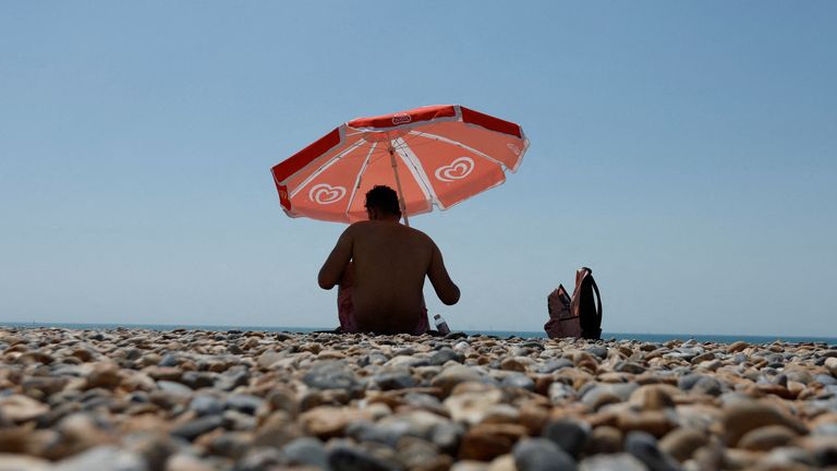 A man sits under an umbrella on Brighton beach, during a heatwave in Brighton, Britain, July 19, 2022. REUTERS/Peter Cziborra