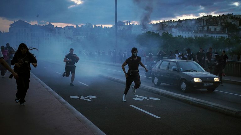 People run away during clashes with police in the center of Lyon, central France, Friday, June 30, 2023. French President Emmanuel Macron urged parents Friday to keep teenagers at home and proposed restrictions on social media to quell rioting spreading across France over the fatal police shooting of a 17-year-old driver. Writing on wall reads in French "Justice for Nahel" (AP Photo/Laurent Cipriani)