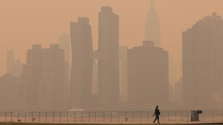 A woman walks along the East River in Long Island as haze and smoke caused by wildfires in Canada hang over the Manhattan skyline, in New York City, New York, U.S., June 7, 2023. REUTERS/Andrew Kelly
