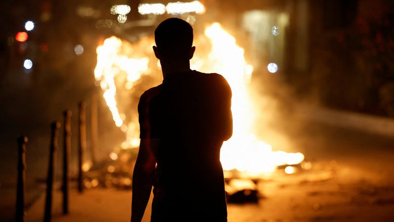 A person stands near a burning container as people protest following the death of Nahel, a 17-year-old teenager killed by a French police officer in Nanterre during a traffic stop, and against police violence, in Paris, France, June 30, 2023. REUTERS/Juan Medina
