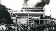 Aug. 08, 1973 - 42 die in the Isle of Man Fun Center Holiday Blaze: The death toll in the Isle of Man holiday blaze rose to 41 today and there are fears that the final figure would reach 50. Firemen continued their search of the ruins which had once been the £2 million Summerland fun center at Douglas, the island's capital. The blaze last night was at the peak of the Island's holiday season. Photo shows Holiday makers look on as clouds of smoke and flames pour out from the Summerland fun c