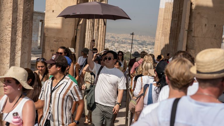 A man holds an umbrella as he and other tourists enters the ancient Acropolis hill during a heat wave, in Athens, Greece, Thursday, July 13, 2023. (AP Photo/Petros Giannakouris)