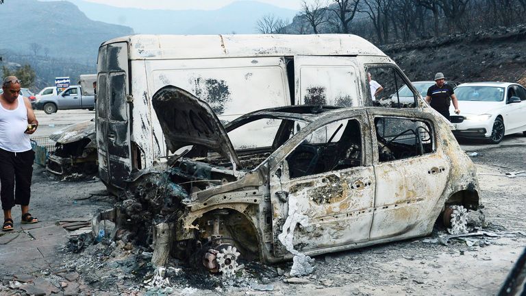 Cezayir, Cezayir'e 100 km uzaklıktaki Bouira'da insanlar orman yangınlarından sonra yanmış araçları inceliyor Pic:AP